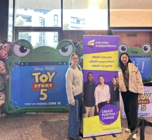 Group of people posing in front of colorful Toy Story-themed backdrops and a purple Everyday Independence banner outside a building.