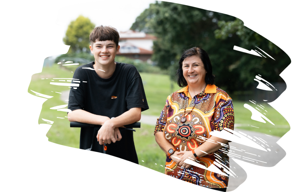 Smiling teenage boy and an adult woman standing together in a park on a sunny day, posing for the photo.
