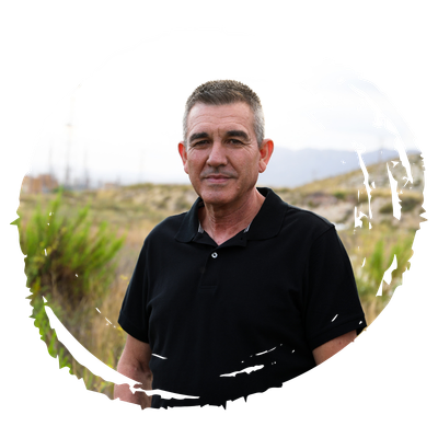 Man in a black polo shirt stands in a dry grassy field with hills in the background.