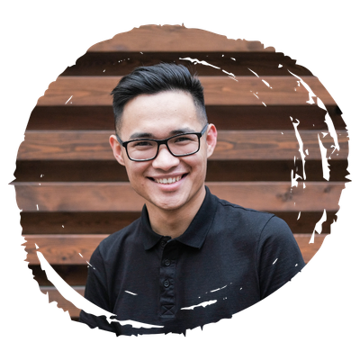 Portrait of a smiling man wearing glasses and a black polo shirt, standing in front of wooden steps.